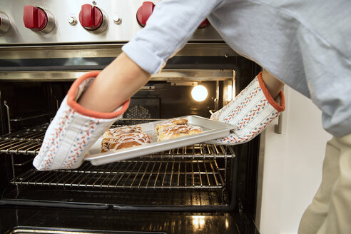 Smiling boy taking baking tray out of the oven with father in background - MFRF01075