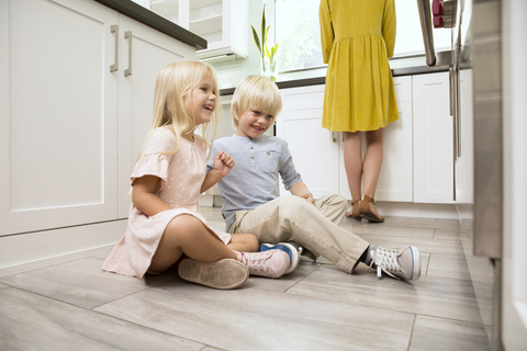 Brother and sister sitting on the floor in kitchen looking at oven stock photo