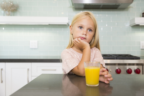 Portrait of pensive girl in kitchen with glass of orange juice stock photo