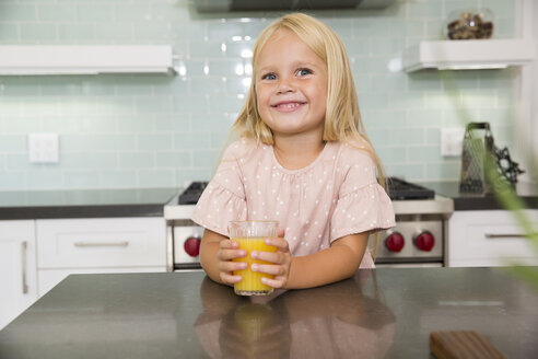 Portrait of smiling girl in kitchen with glass of orange juice - MFRF01086