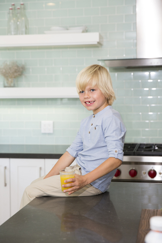 Happy boy in kitchen with glass of orange juice stock photo