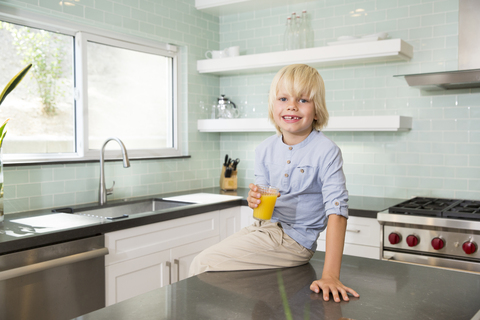 Porträt eines glücklichen Jungen in der Küche mit einem Glas Orangensaft, lizenzfreies Stockfoto