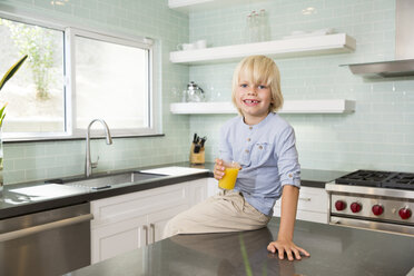 Porträt eines glücklichen Jungen in der Küche mit einem Glas Orangensaft - MFRF01089
