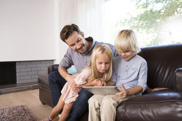 Father and son sitting on couch at home using tablet - MFRF01103