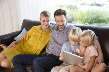 Family sitting on couch at home using tablet - MFRF01105