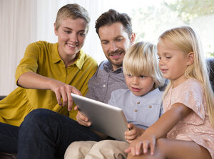 Familie sitzt zu Hause auf der Couch und benutzt ein Tablet - MFRF01106