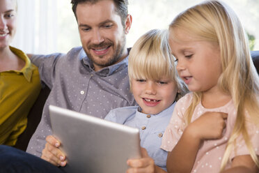 Family sitting on couch at home using tablet - MFRF01107