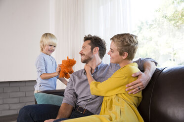 Eltern, die sich zu Hause auf der Couch umarmen und ein Junge, der mit einem Kuscheltier spielt - MFRF01109