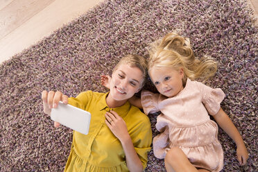 Lächelnde Mutter und Tochter liegen auf dem Teppich und machen ein Selfie - MFRF01110