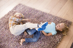 Verspielte Geschwister, die zu Hause auf dem Teppich liegen - MFRF01112