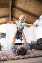 Vater spielt mit Tochter auf Teppich im Wohnzimmer zu Hause - MFRF01114