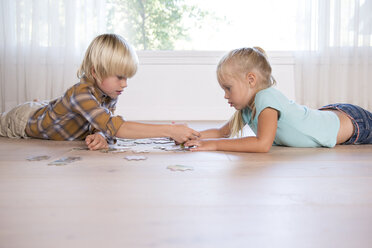 Bruder und Schwester liegen zu Hause auf dem Boden und spielen ein Puzzle - MFRF01119