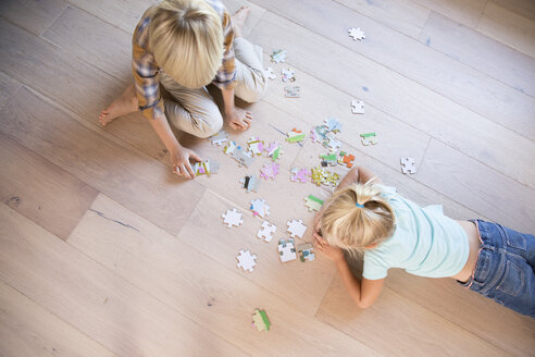 Brother and sister lying on the floor at home playing jigsaw puzzle - MFRF01120