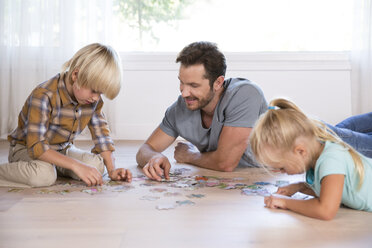 Father with two children lying on the floor at home playing jigsaw puzzle - MFRF01121
