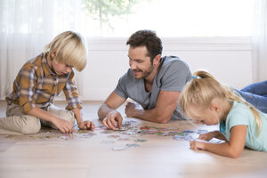 Vater mit zwei Kindern, die zu Hause auf dem Boden liegen und Puzzle spielen - MFRF01121