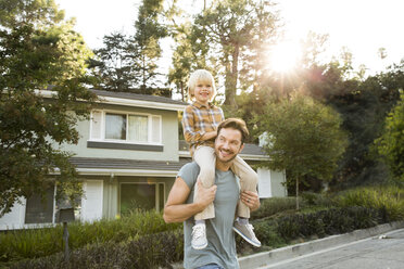 Happy boy on father's shoulders in front of their home - MFRF01128