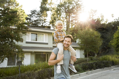 Happy boy on father's shoulders in front of their home - MFRF01128