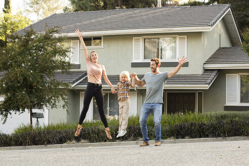 Happy family with son jumping in front of their home - MFRF01135