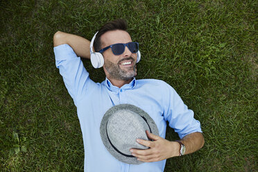 Portrait of laughing man relaxing on a meadow listening music with headphones, top view - BSZF00138