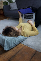 Young woman lying on the floor at home using laptop - HHLMF00061
