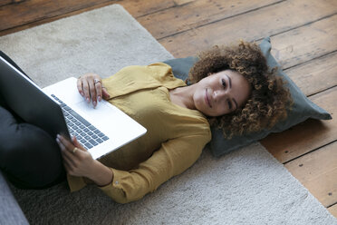Smiling young woman lying on the floor at home with laptop - HHLMF00062