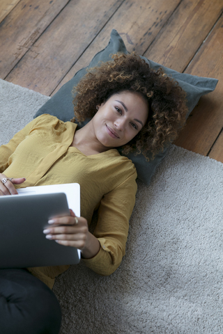Lächelnde junge Frau zu Hause auf dem Boden liegend mit Laptop, lizenzfreies Stockfoto