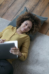 Lächelnde junge Frau zu Hause auf dem Boden liegend mit Laptop - HHLMF00063