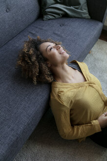 Smiling young woman leaning on couch at home - HHLMF00065