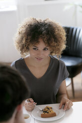 Smiling young woman eating cake at table looking at man - HHLMF00071