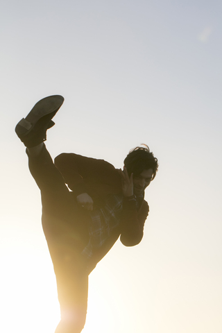 Junger Mann macht eine Kickboxbewegung im Freien bei Sonnenuntergang, lizenzfreies Stockfoto