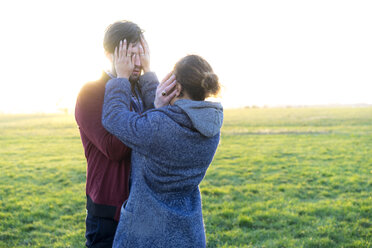 Young couple standing on a meadow covering their eyes - HHLMF00104