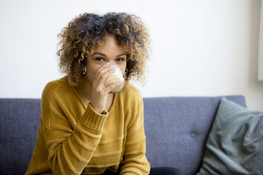 Porrait einer jungen Frau, die zu Hause auf der Couch sitzt und trinkt - HHLMF00110