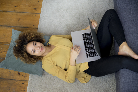 Smiling young woman lying on the floor at home using laptop stock photo