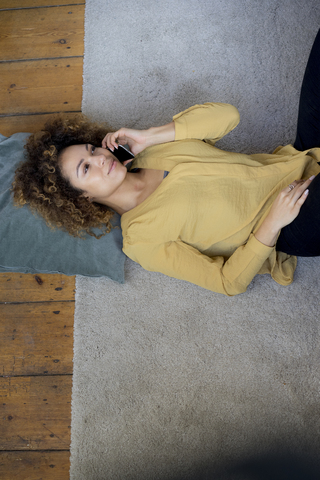 Junge Frau mit Handy auf dem Boden liegend zu Hause, lizenzfreies Stockfoto