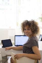 Portrait of smiling young woman at home with laptop and tablet - HHLMF00127