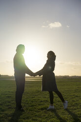 Affectionate young couple standing hand in hand on a meadow at sunset - HHLMF00142