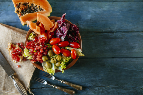Papayasalat, Granatapfel, Kopfsalat, Tomate, Oliven und Endivie auf blauem Holz, lizenzfreies Stockfoto