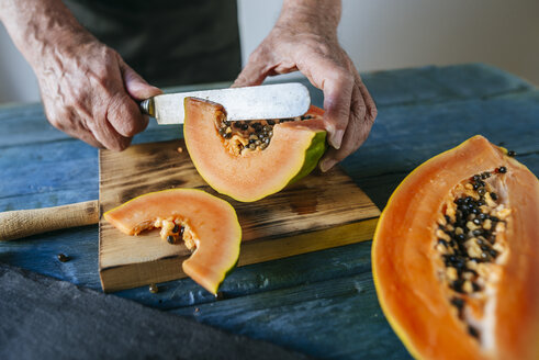 Hände eines älteren Mannes beim Schneiden von Papaya - KIJF01824