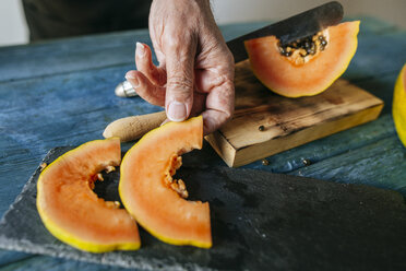 Nahaufnahme der Hände eines Mannes, der Papayastücke auf eine Schieferplatte legt - KIJF01825