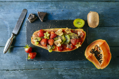 Halbe Papaya, dekoriert mit Bananenstücken, Kiwi und Erdbeeren auf einer Schieferplatte, lizenzfreies Stockfoto