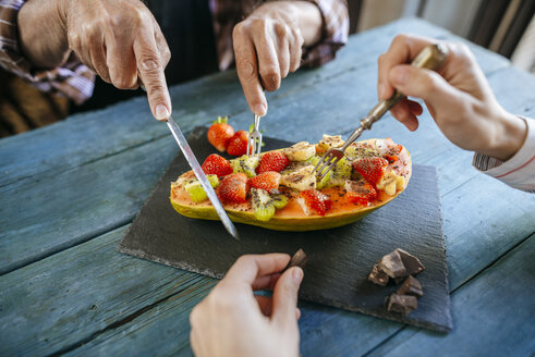 Nahaufnahme der Hände eines Mannes und einer Frau, die Papaya mit Kiwi, Banane und Erdbeeren essen - KIJF01836