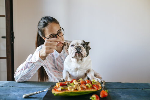 Frau füttert französische Bulldogge am Tisch - KIJF01837