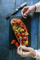 Nahaufnahme von Frauenhänden, die Papaya mit Kiwi, Banane und Erdbeeren essen - KIJF01839