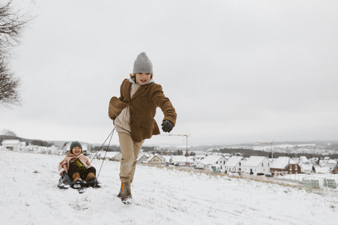 Boy pulling sledge with little sister in snow stock photo