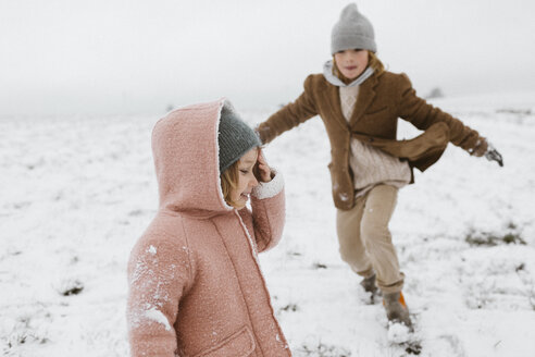 Glückliches kleines Mädchen im Schnee mit spielendem Bruder im Hintergrund - KMKF00112