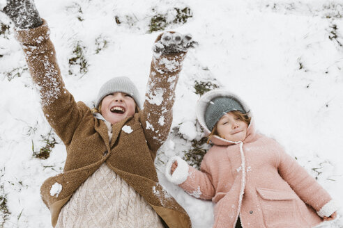 Brother and little sister lying side by side on snow-covered meadow - KMKF00116