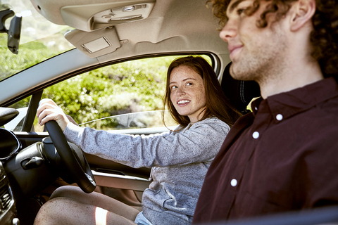 Smiling young woman driving car looking at her boyfriend stock photo