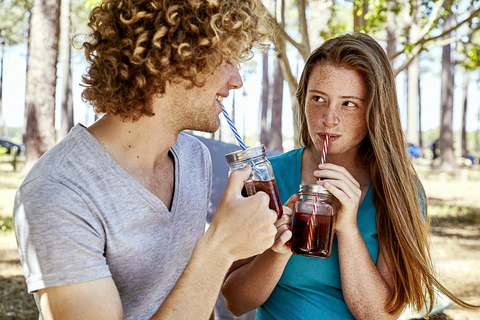 Lächelndes junges Paar bei einem Drink im Wald, lizenzfreies Stockfoto