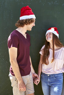 Young couple wearing Christmas hats smiling at each other - SRYF00711