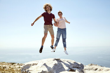 Südafrika, Kapstadt, glückliches junges Paar beim Sprung auf einen Berg an der Küste - SRYF00744